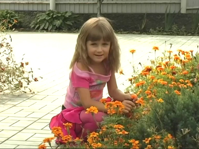 ピンクのフリフリスカートを履いた洋ロリジュニアアイドルマリヤちゃんが花壇の前で座って微笑んでいる